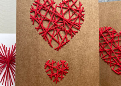 Drei DIY-Herzen aus rotem Faden in eine Karte gestrickt